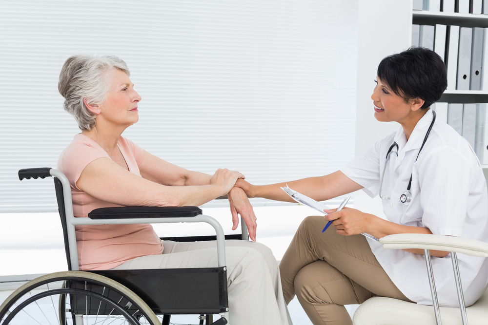 Side view of a doctor talking to a senior patient in wheelchair at the hospital